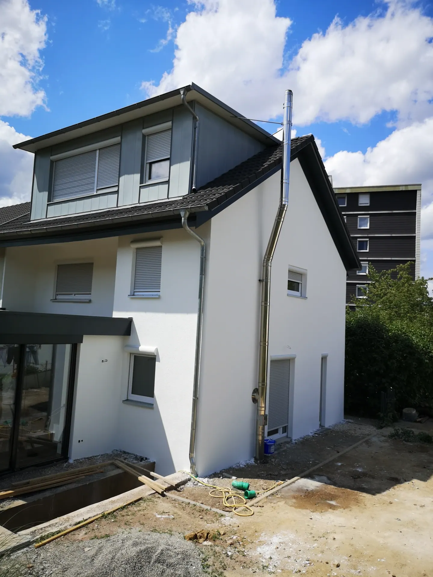 Ansicht des überarbeiteten Hauses mit heller Fassade und grauer Dachgaube
